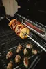 A rotisserie spit with pineapple and jalapeño poppers on a grill. Produktbild-Vorschau