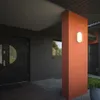 An outdoor wall lamp is mounted on an orange pillar next to a dark gray brick house with a double door. Produktbild-Vorschau