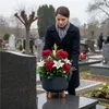 A woman places a flower arrangement in a pot on a tombstone in a cemetery. Podgląd zdjęcia produktu