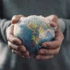 Hands holding a small globe wrapped in bubble wrap. Produktbild-Vorschau