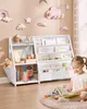 A young girl is reading a book in front of a white bookshelf filled with children's books and toys, in a room decorated with cloud and rainbow wall art. Produktbild-Vorschau