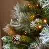 A close-up view of a decorated Christmas tree with pine needles, pinecones, and warm white lights. Podgląd zdjęcia produktu