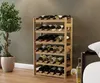 A wooden wine rack filled with wine bottles, placed next to a potted plant and a sofa in a room. Náhled obrázku produktu