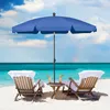 Two lounge chairs with towels and drinks on a sandy beach under a blue umbrella, with the ocean in the background. Produktbild-Vorschau