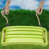 A close-up view of a green plastic swing seat with ropes attached, set against a blurred green hedge and blue sky background. Anteprima dell’immagine prodotto