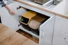 A person is putting a plastic bottle into a recycling bin system under a kitchen counter. Produktbild-Vorschau