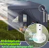 A dark gray party tent set up in a grassy field, with sunlight rays shining on it. Inside the tent, a campfire is burning, and two people are sitting. Produktbild-Vorschau