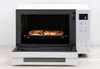 A white Panasonic combi microwave oven with its door open, showing a pizza inside. Produktbild-Vorschau