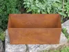 A rusty metal planter box sits on large stones in a garden setting with green foliage in the background. Anteprima dell’immagine prodotto