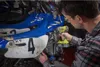 A man is using a cordless drill to work on a dirt bike in a garage. Produktbild-Vorschau