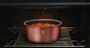 A copper pot filled with food is placed on a rack inside a dark oven. Podgląd zdjęcia produktu