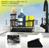 A black metal sink caddy holding a blue soap dispenser, yellow sponges, and brushes, placed on a kitchen sink next to a black faucet. Produktbild-Vorschau