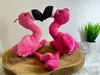 Two plush flamingo toys are positioned on a wooden surface. Produktbild-Vorschau