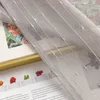 A close-up of a sheer gray curtain with white embroidered stripes and dots, partially obscuring a framed picture of flowers and an open book with illustrations of potted plants and text. Produktbild-Vorschau