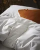 A close-up view of a neatly made bed with white bedding and an orange accent pillow. Produktbild-Vorschau