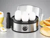 An egg cooker with eggs inside, along with a soft-boiled egg in an egg cup and some bread rolls on a countertop. Produktbild-Vorschau
