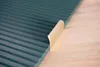 A close-up of a dark green ribbed surface with a beige curved edge detail, placed on a light wooden surface. Produktbild-Vorschau