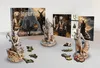 A tabletop display of board game components, including miniatures, cards, and a game box. Náhled obrázku produktu