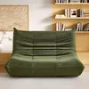 A green sofa is placed in a living room setting with bookshelves in the background. Produktbild-Vorschau