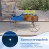 A blue wooden garden cart planter with plants and soil, shown outdoors on a paved surface with a stone wall and greenery in the background. A close-up inset highlights a drainage hole. Produktbild-Vorschau