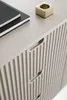 A close-up view of a dresser with ribbed fronts and a drawer pull. Two notebooks and a small brass object are on top. Náhled obrázku produktu