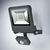 A dark gray LED floodlight with a motion sensor is mounted on a light gray wall. Produktbild-Vorschau
