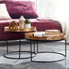 Two round coffee tables with gold hammered tops and black metal frames are placed in a living room setting, in front of a plush purple sofa.