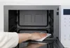 A hand is wiping the inside of a microwave with a white cloth. Produktbild-Vorschau