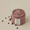 A jar of pink pore mask with red beans scattered around it on a light beige background. Produktbild-Vorschau