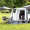 A camping setup with a van, an attached awning tent, and outdoor furniture. Produktbild-Vorschau