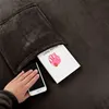 A close-up view of a hand holding a smartphone, with a book tucked into the pocket of a dark brown blanket. Podgląd zdjęcia produktu