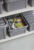 Several gray storage boxes are stacked on a shelf, with one box open and filled with fishing lures. Anteprima dell’immagine prodotto