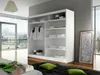 A modern bedroom with a large white wardrobe, a bed with green pillows and a blanket, and a large window overlooking a city. Produktbild-Vorschau