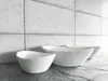 Three white oval washbasins are arranged on a textured surface in front of a tiled wall. Náhled obrázku produktu