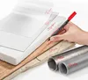 A hand holding a black and red marker writing on different materials like film, glass, styrofoam, wood, stone, metal, and plastic. Produktbild-Vorschau