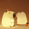 Two illuminated capybara-shaped night lights are placed on a brown surface. Produktbild-Vorschau