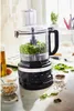 A black KitchenAid food processor is shown on a kitchen counter, filled with chopped green ingredients. Several small bowls containing nuts, seeds, and spices are arranged around it, along with fresh spinach leaves. Anteprima dell’immagine prodotto