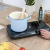 A person's hand is operating a portable double induction hob, which has a light blue pot on the left burner and a wooden spoon inside. Náhľad obrázku produktu