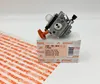 A STIHL carburetor is placed on top of its original packaging box, with a roll of STIHL branded wrapping paper in the foreground. Produktbild-Vorschau
