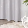 A close-up view of a light gray curtain with silver wavy stripes and small dots, placed on a wooden floor next to a fluffy beige rug and two white decorative vases. Produktbild-Vorschau