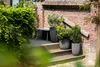 Three planters with plants on a set of wooden steps next to a brick wall. Náhľad obrázku produktu