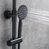 A close-up shot of a black showerhead system mounted on a tiled wall, with water spraying from the showerhead. Produktbild-Vorschau