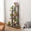 A multi-tiered plant stand with various potted plants is placed in a living room setting next to a sofa and armchair. Náhled obrázku produktu