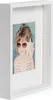 A white shadow box frame with a photo of a young girl wearing sunglasses and holding a seashell. Produktbild-Vorschau