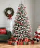 A festive Christmas scene with a flocked artificial tree, decorated with red and gold ornaments, surrounded by wrapped gifts. A wreath hangs on the wall, and a Santa figure sits to the side. Produktbild-Vorschau