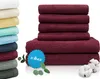 A stack of burgundy towels and a stack of multi-colored towels, with a small sprig of eucalyptus and cotton bolls. Produktbild-Vorschau