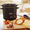 A black Russell Hobbs slow cooker is shown on a wooden cutting board with ingredients for a meal, including tomatoes, garlic, onions, cheese, and lasagna sheets. Podgląd zdjęcia produktu