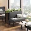 A modern waiting area with two gray upholstered benches, coffee tables, and potted plants near a large window with a city view. Podgląd zdjęcia produktu