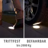 A split image showing a person stepping on a ground light and a car tire pressing on another ground light, demonstrating durability. Produktbild-Vorschau