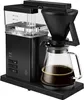 A black Melitta coffee maker with a glass carafe filled with coffee, shown on a black base. Produktbild-Vorschau